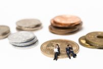 お金の硬貨の上に座って仕事に悩む人間