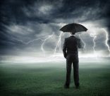 risk and crisis – businessman below storm with umbrella