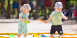 Two baby boys playing with sand in a sandbox