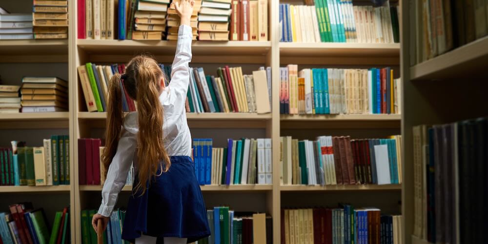 Rear,View,On,Little,Pupil,Girl,In,Library,Taking,A
